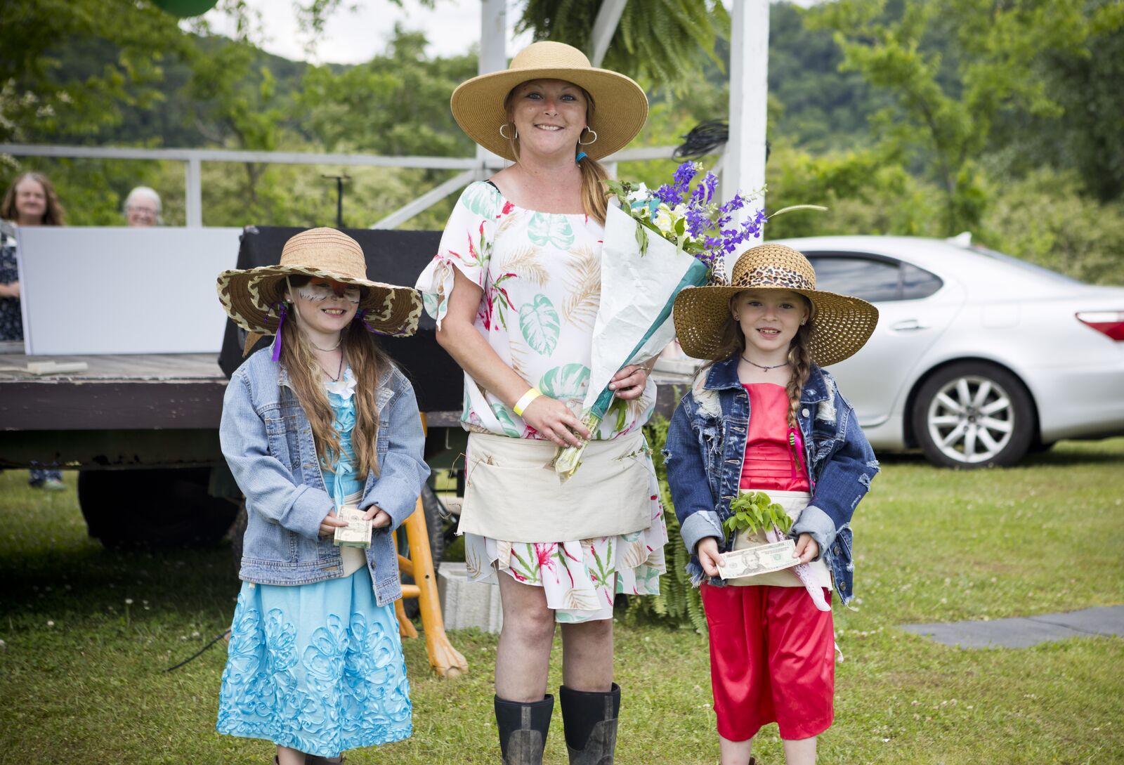 Contest winners in straw hats holding flowers and prizes beside the festival stage