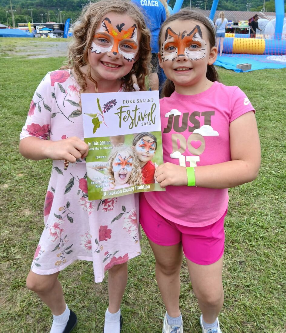Two girls with fox face paint holding a Poke Sallet Festival program